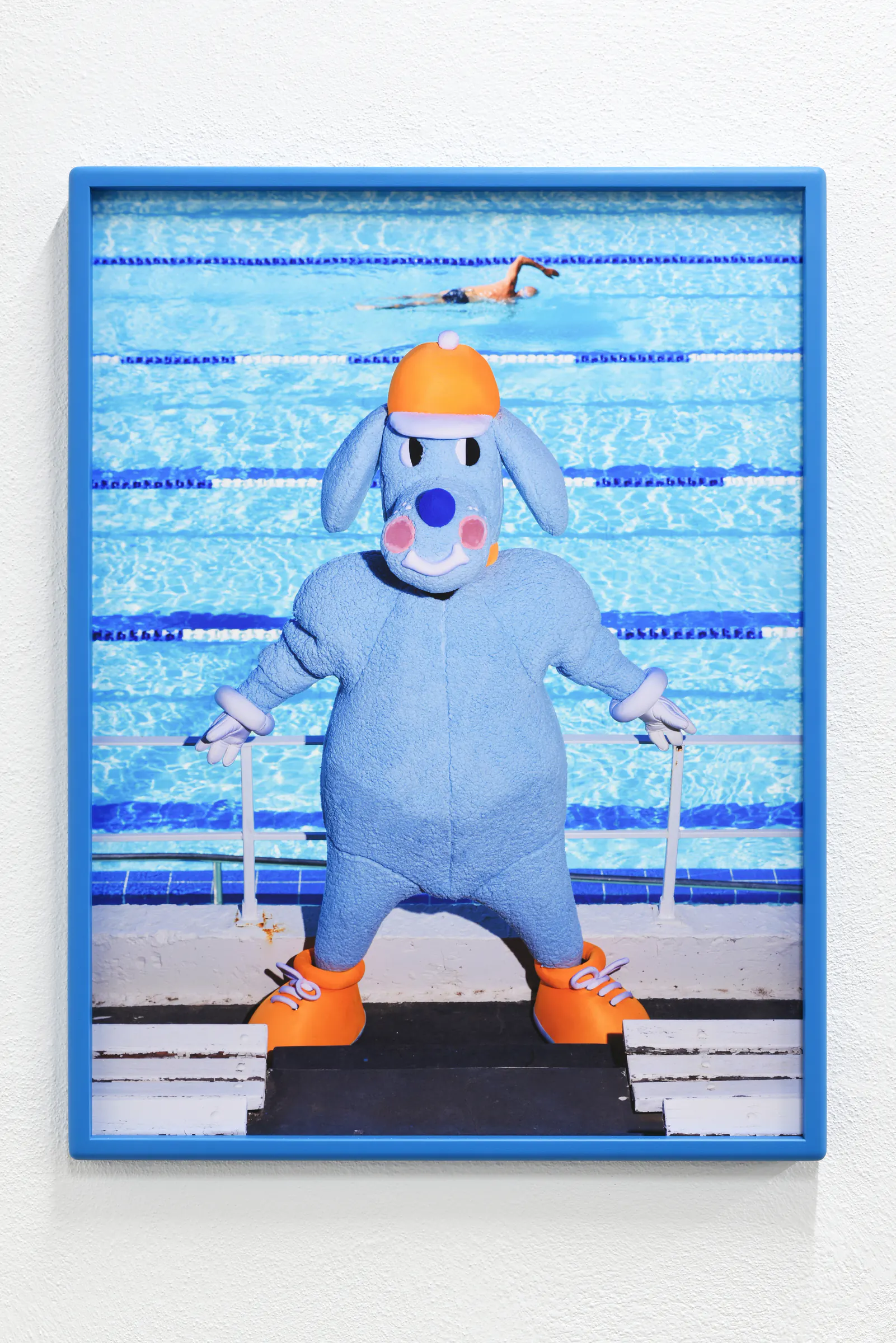 Framed photograph of the blue Sports Dreams mascot, installed in the gallery